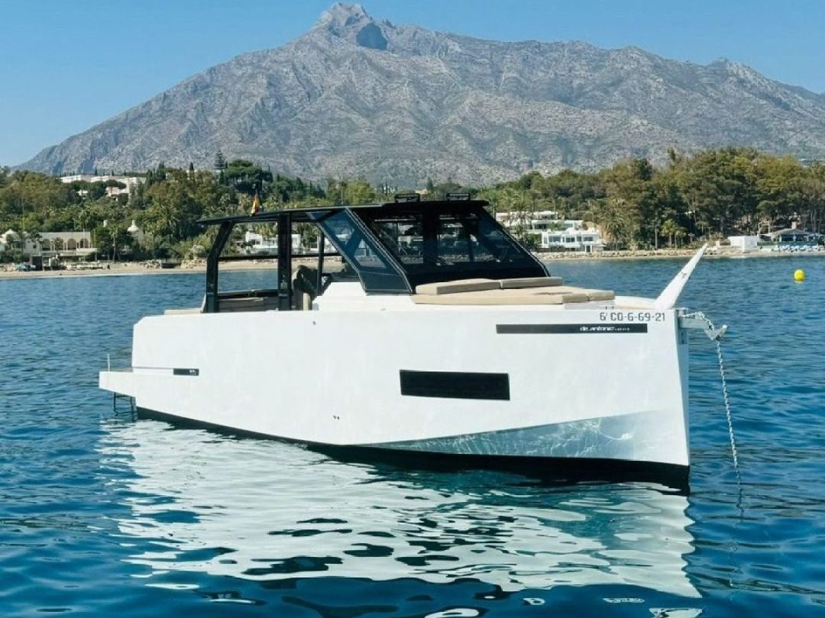 A white modern boat on blue water with a large mountain in the background.