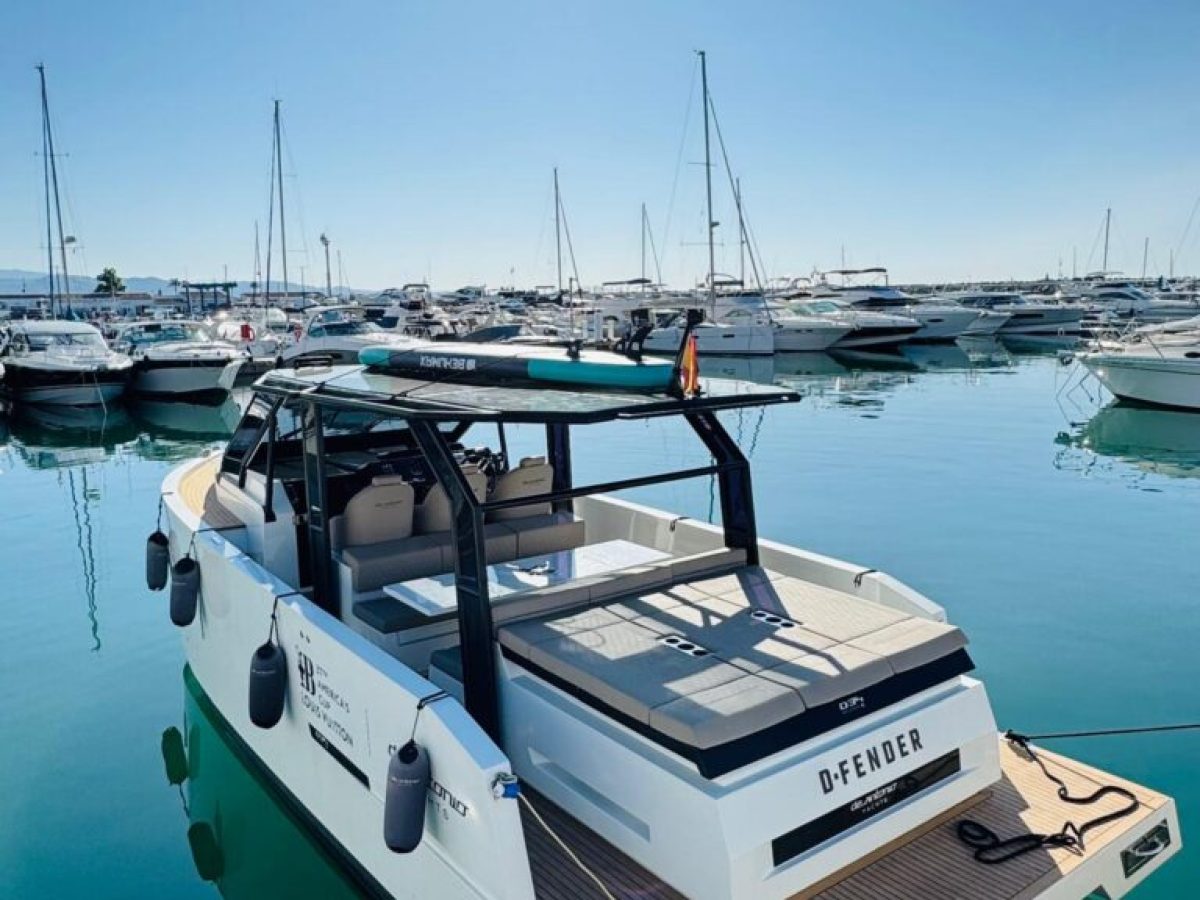 Modern boat with sunroof docked in a sunny marina, surrounded by several other boats.