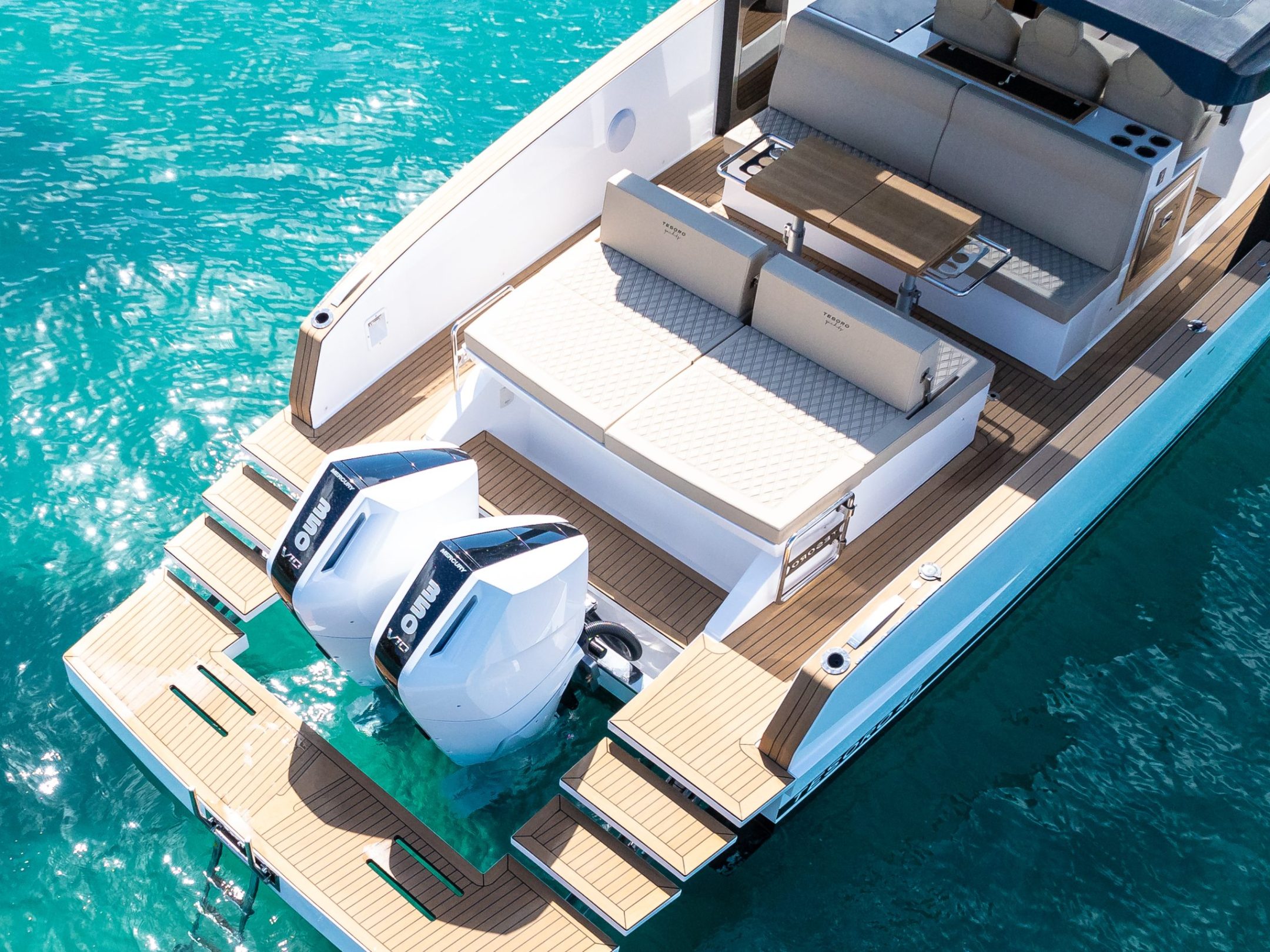 Top view of a motorboat with twin outboard engines on clear blue water.
