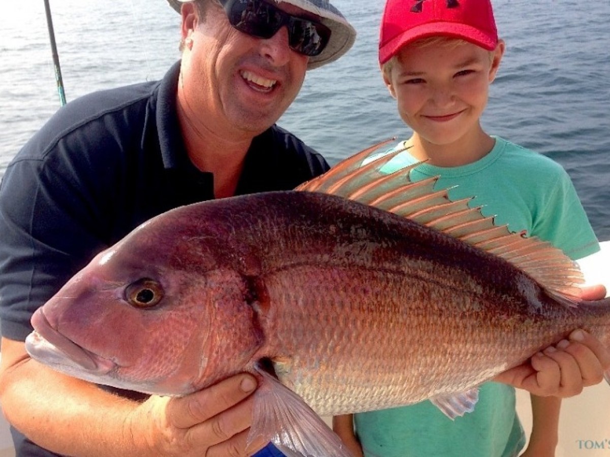 Man and child holding large fish on boat, smiling, ocean in background.