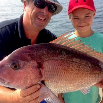 Two people holding a large fish on a boat, with water in the background.
