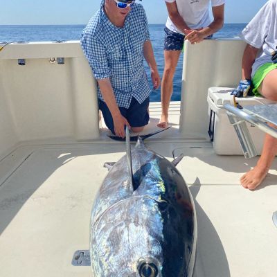 Two men on a boat with a large tuna fish on deck.