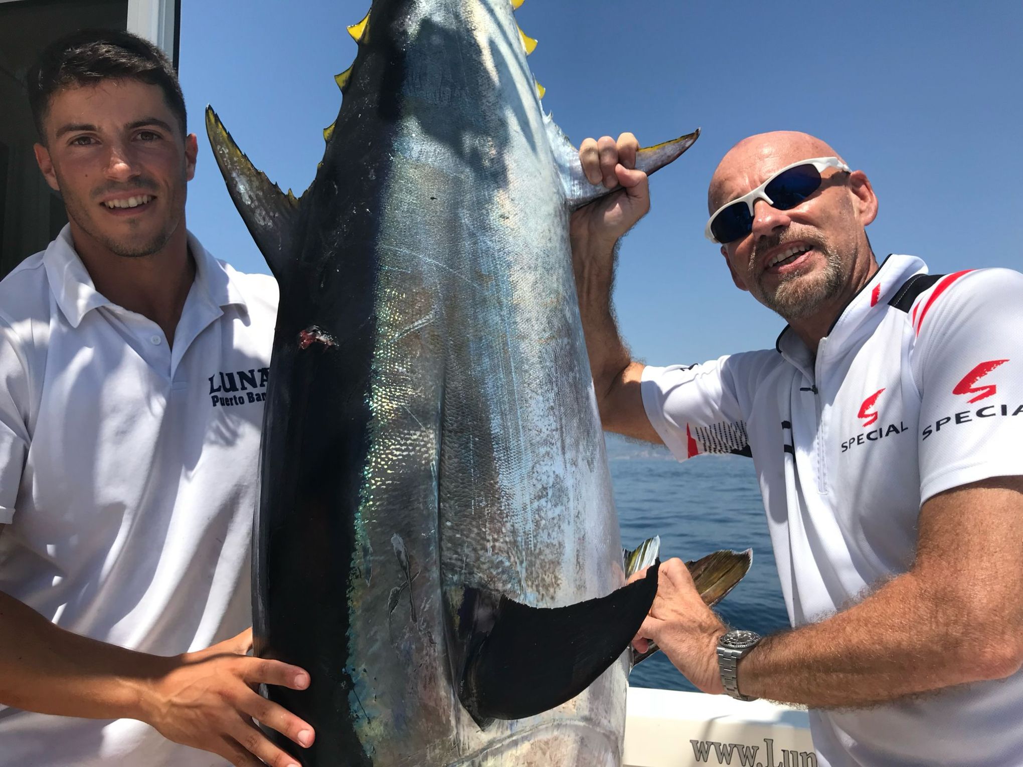 Two men proudly holding a large tuna fish on a boat at sea.