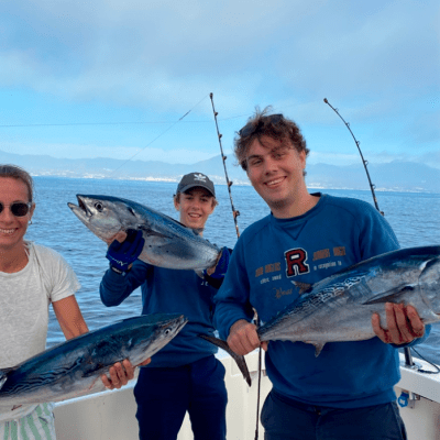 Three people on a boat holding fish with rods in the background over a calm sea.
