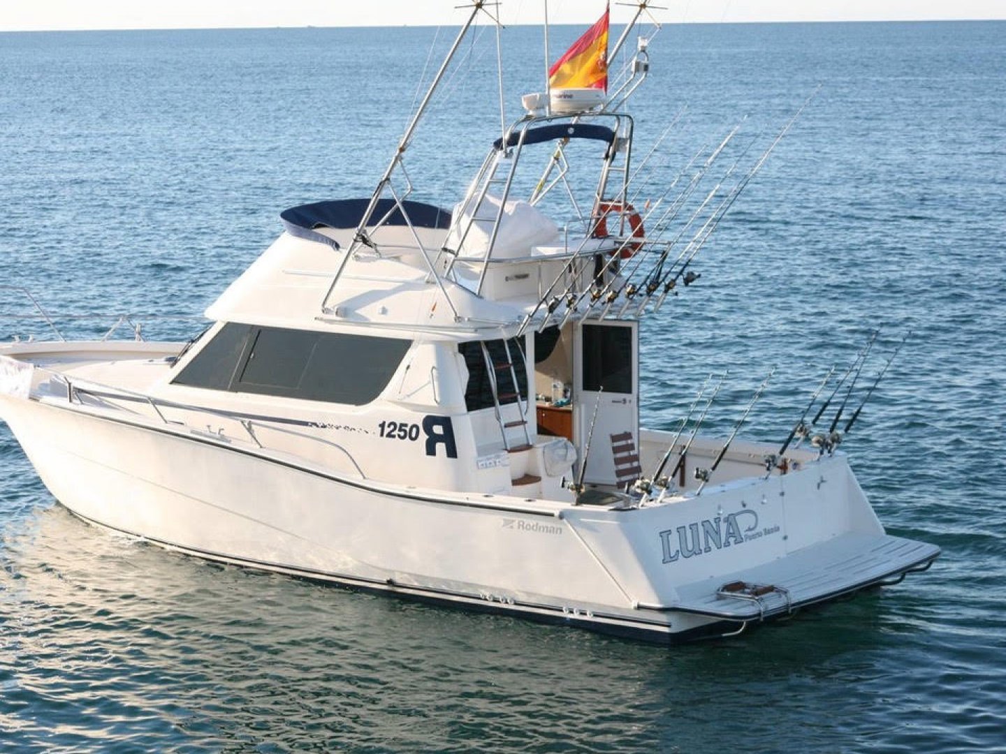 A white fishing boat named LUNA on water with fishing rods and a flag.