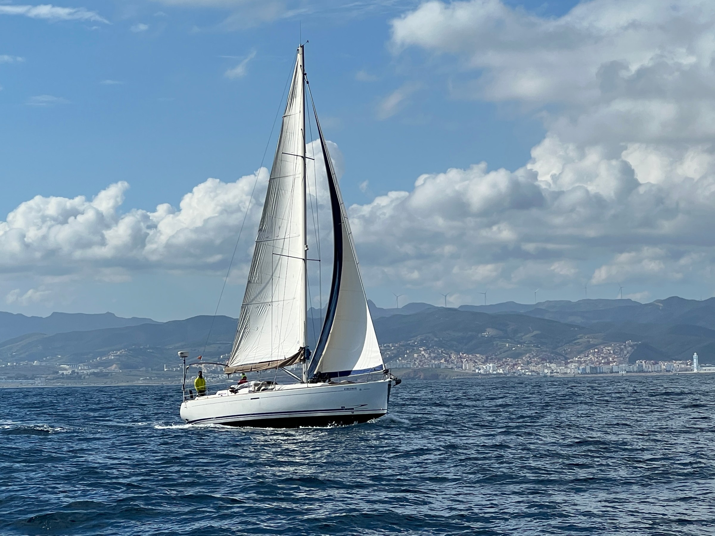 Sailboat on ocean near mountainous coastline under partly cloudy sky.