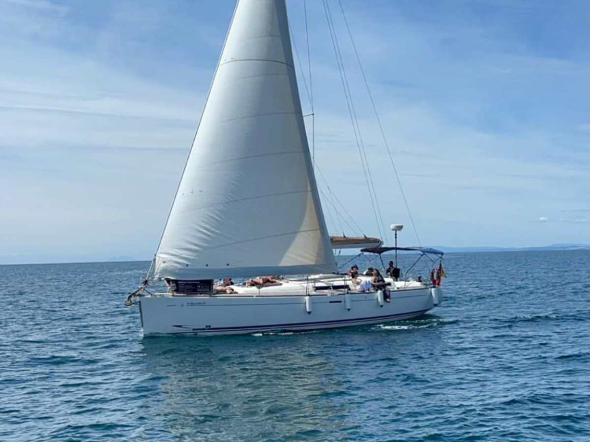 A sailboat with white sails on a calm sea under a clear blue sky.