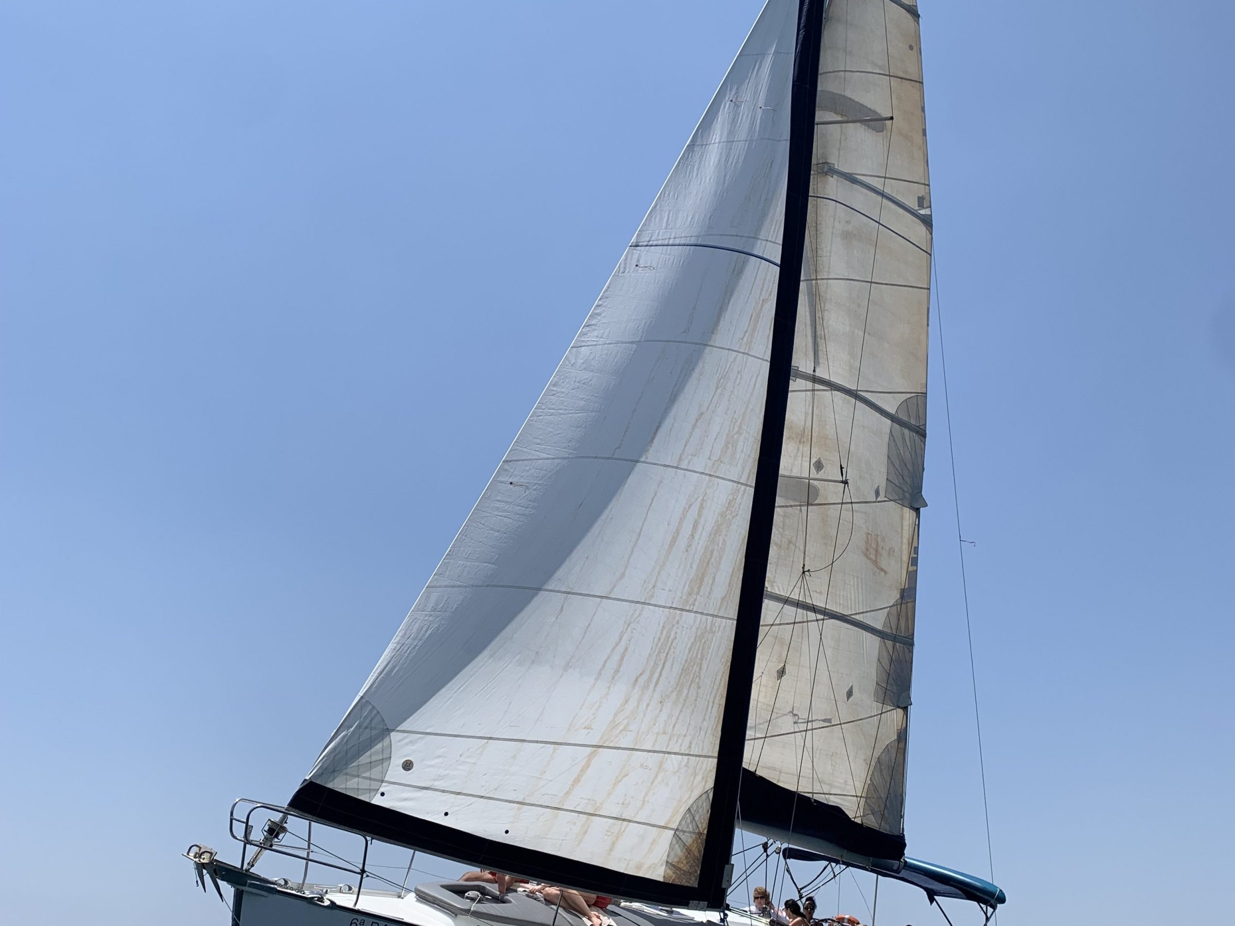 Sailboat with large white sails, sailing on clear blue sea under bright sky.