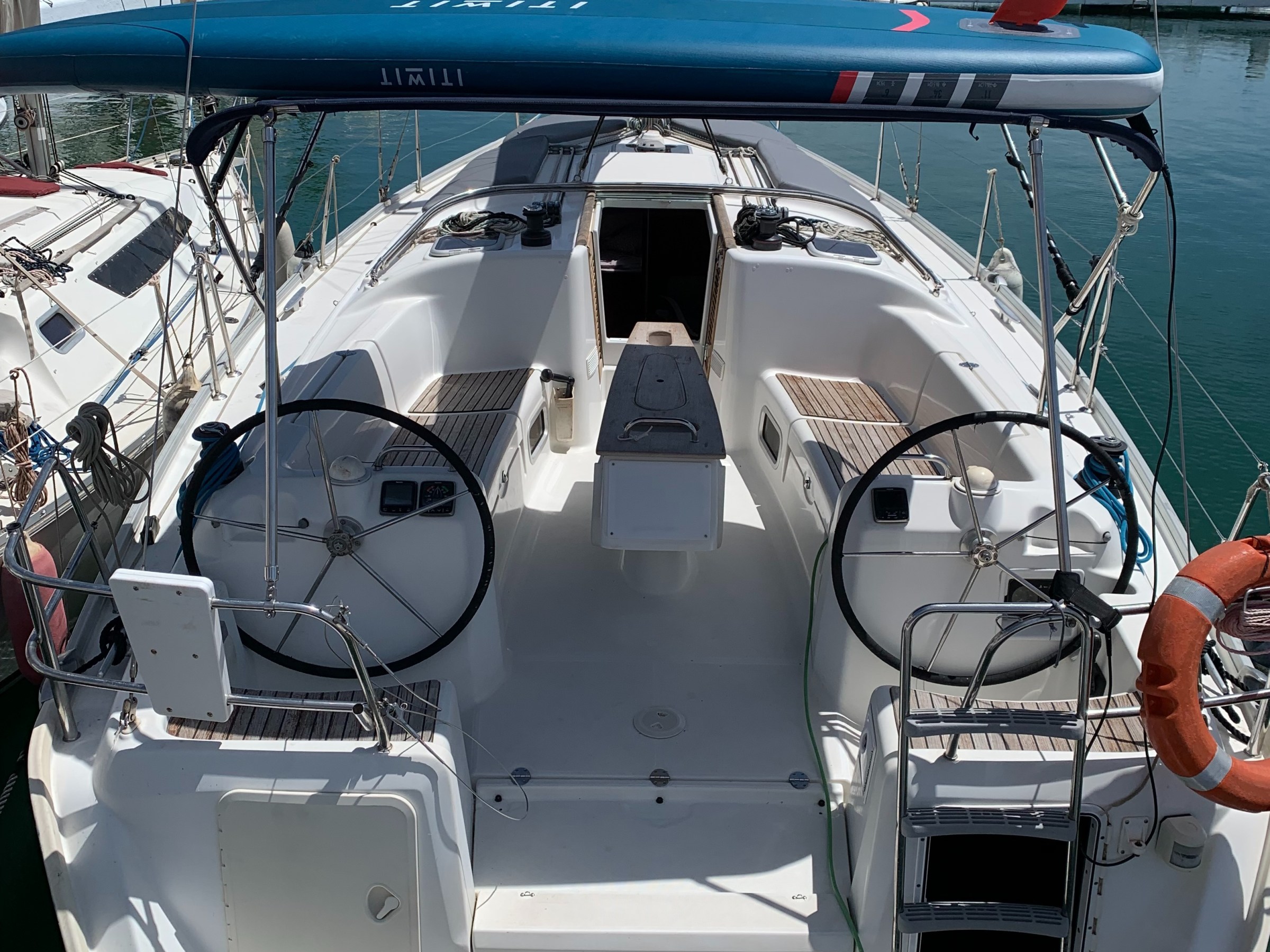 Back view of a docked sailboat with dual steering wheels and a marina in the background.