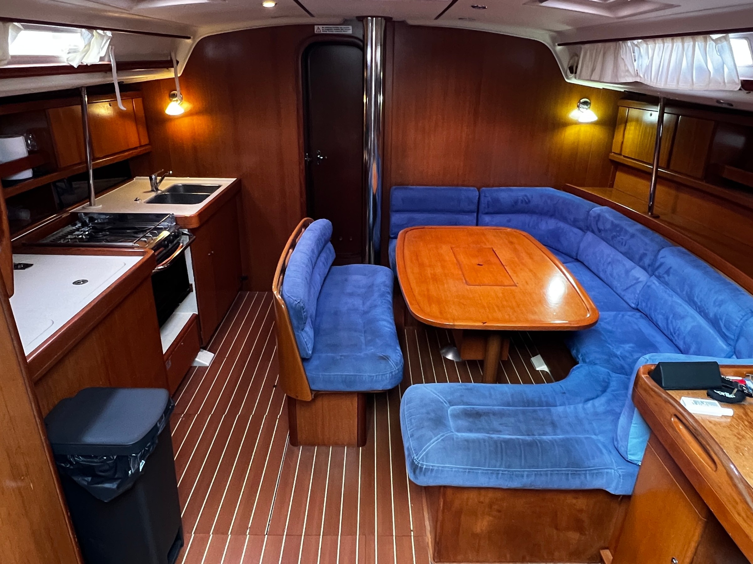 Interior of a yacht with blue cushioned seating, wooden table, and kitchenette.