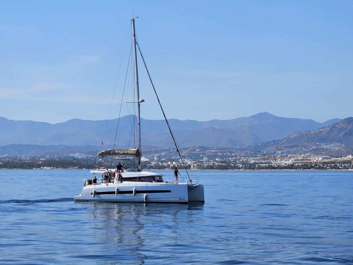 Catamaran sailing on calm sea with mountains in background.