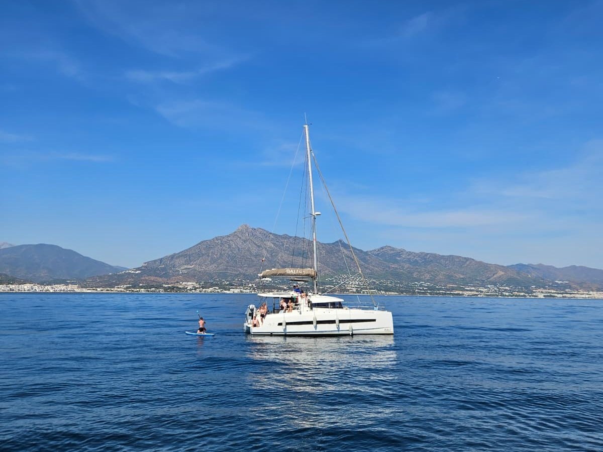Sailboat with people on calm sea near mountains and clear sky.