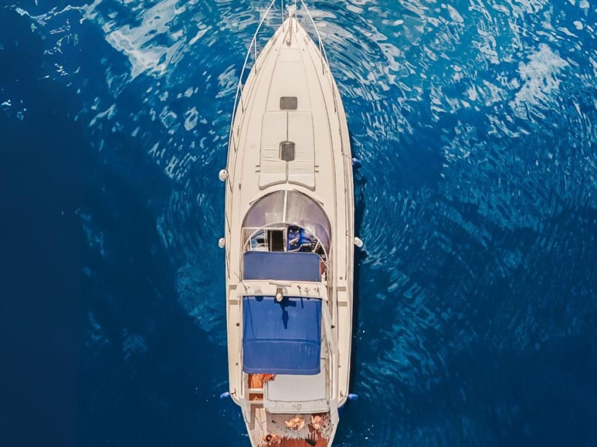 Aerial view of a yacht on blue water with people sunbathing and swimming.