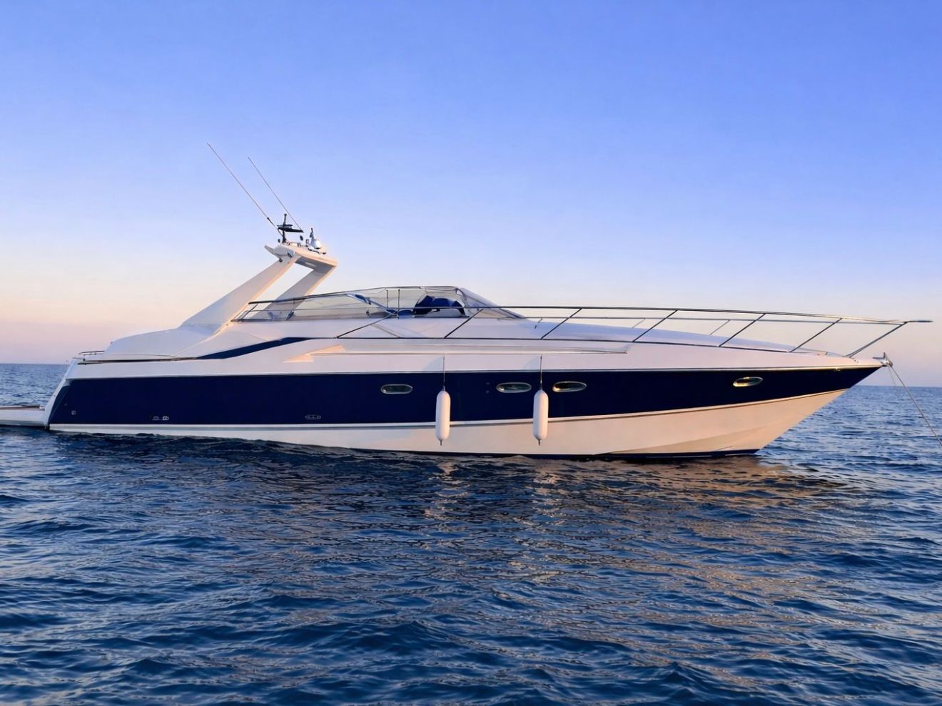 Luxury yacht on calm blue sea under clear sky at sunset.