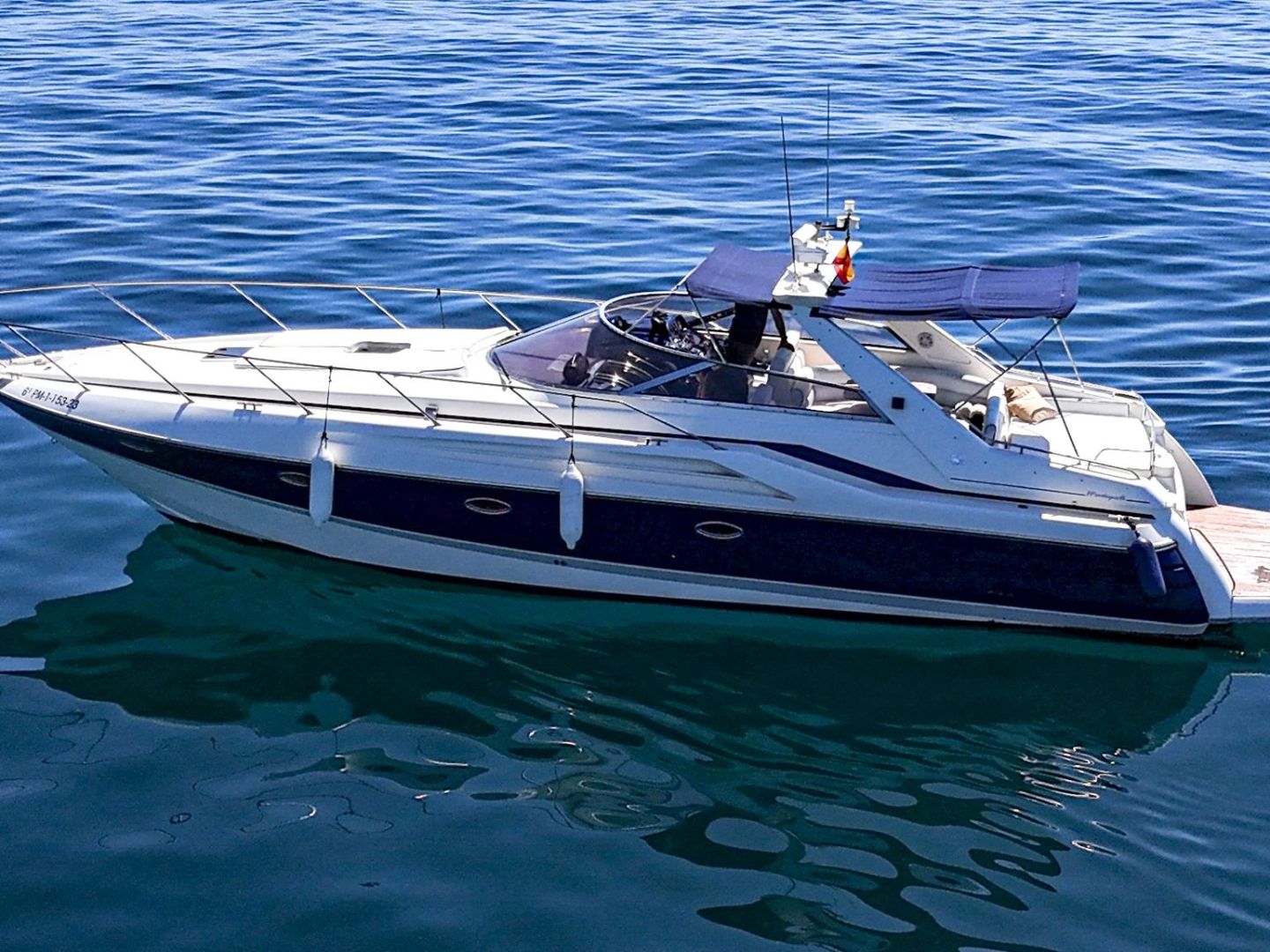 A white yacht with a blue canopy cruising on calm blue waters.