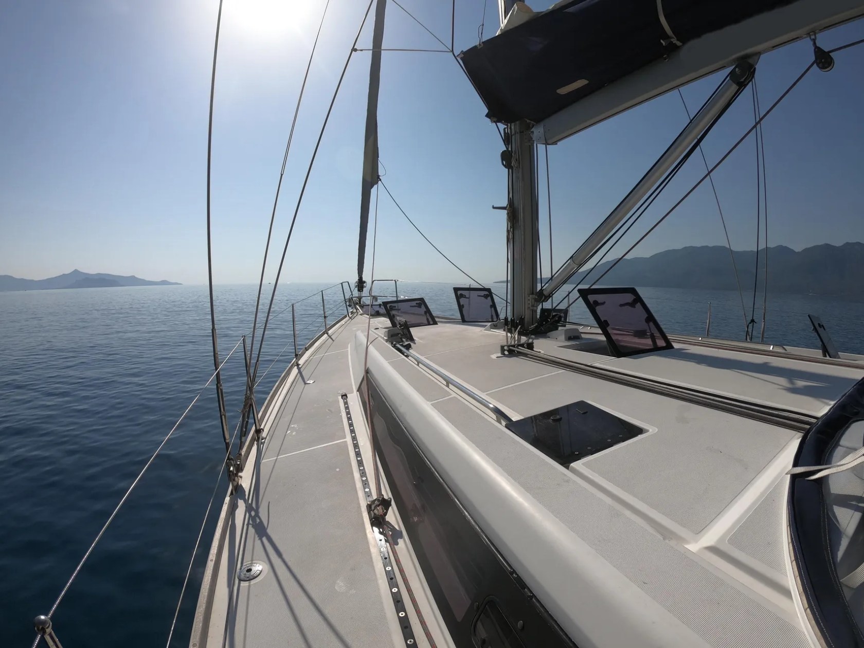 Sailing boat deck with calm sea and distant mountains under clear sky.