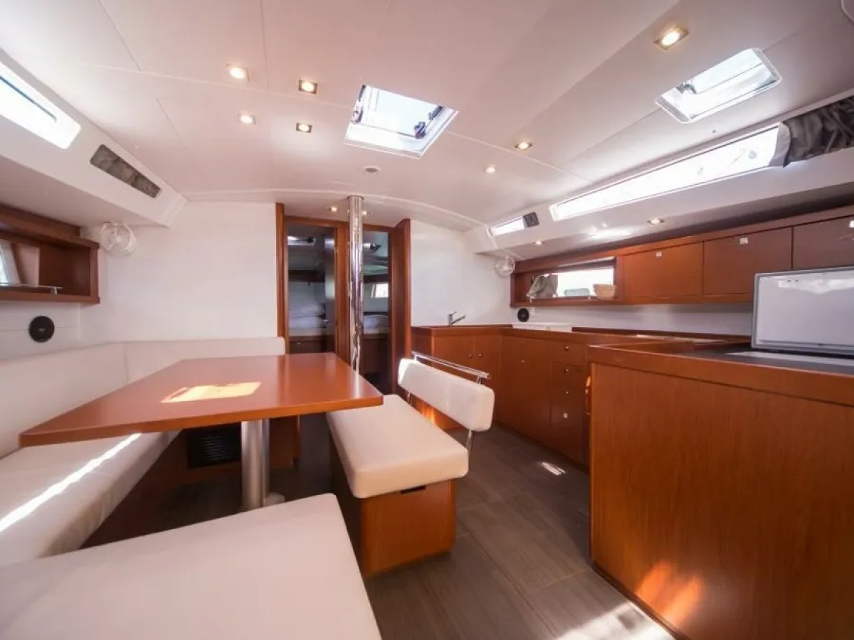 Interior of a yacht with a dining area and kitchen, featuring wooden cabinets and white seating.
