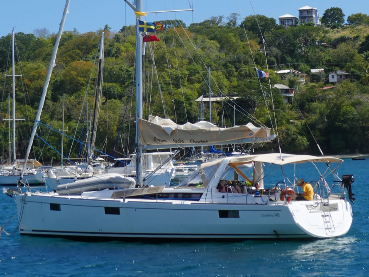Sailboat anchored in blue water near a lush, hilly coastline.