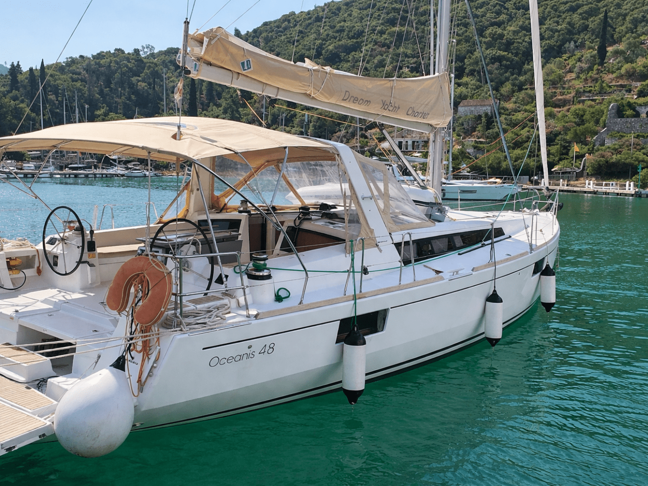 Sailboat docked in marina with hills and greenery in background.