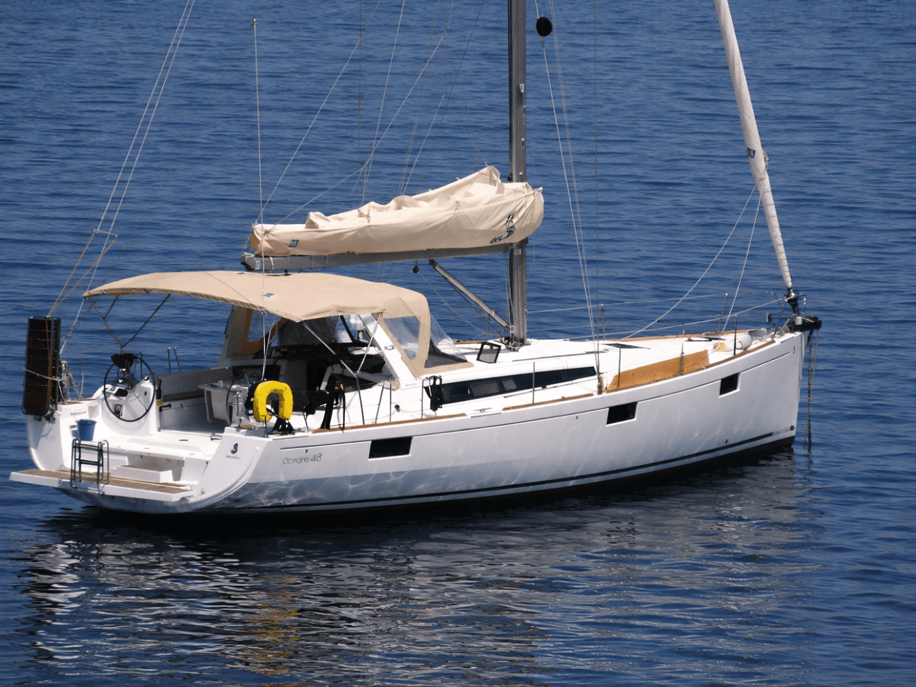White sailboat with beige canopy anchored on calm blue water.