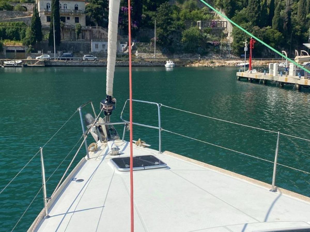 Bow of a sailboat in a marina with greenery and hills in the background.