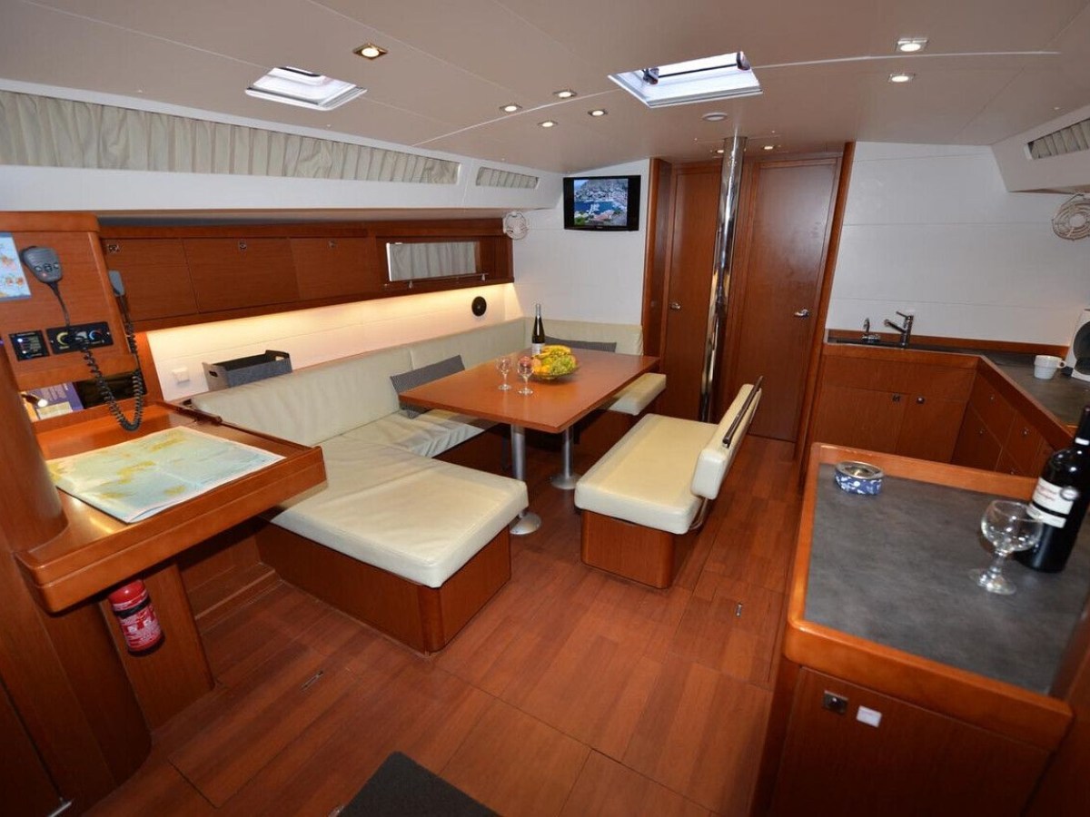 Elegant yacht interior with a seating area, dining table, kitchenette, and wooden furnishings.