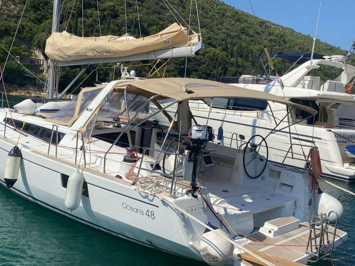 White sailboat docked at a marina with green hills in the background.