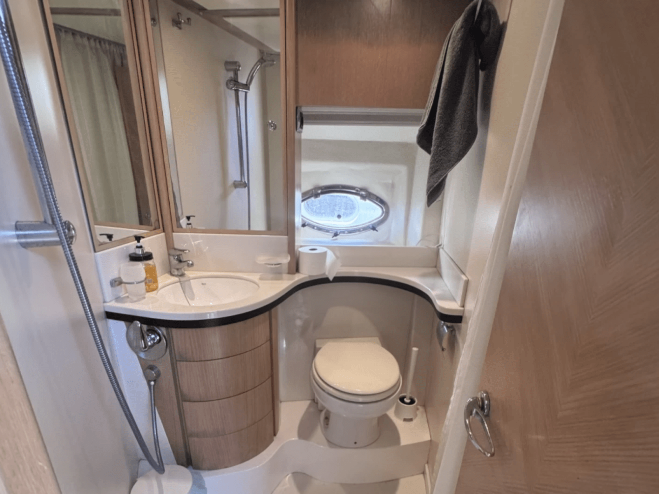 Compact bathroom with sink, toilet, mirror, and towels in a light wood design.