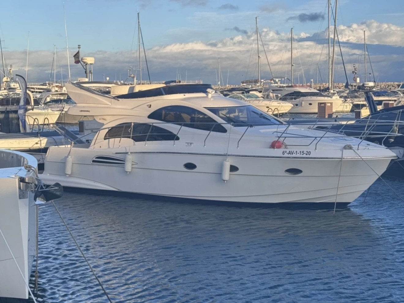 White yacht docked in a marina with other boats.
