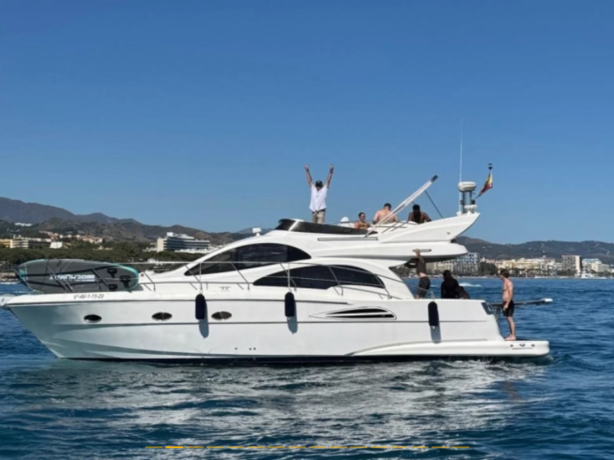 White yacht on blue water with people on deck under a clear sky.