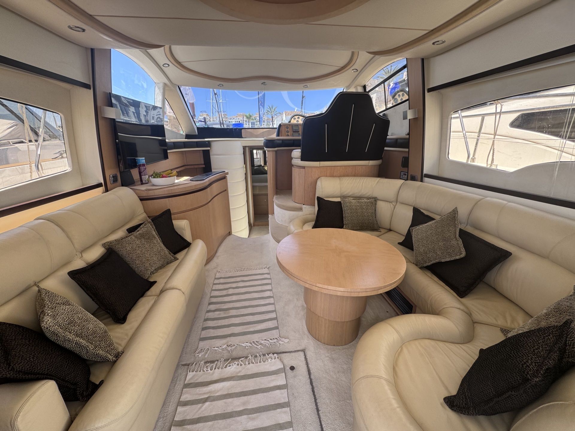 Luxurious yacht interior with beige sofas, black cushions, and a round wooden table.