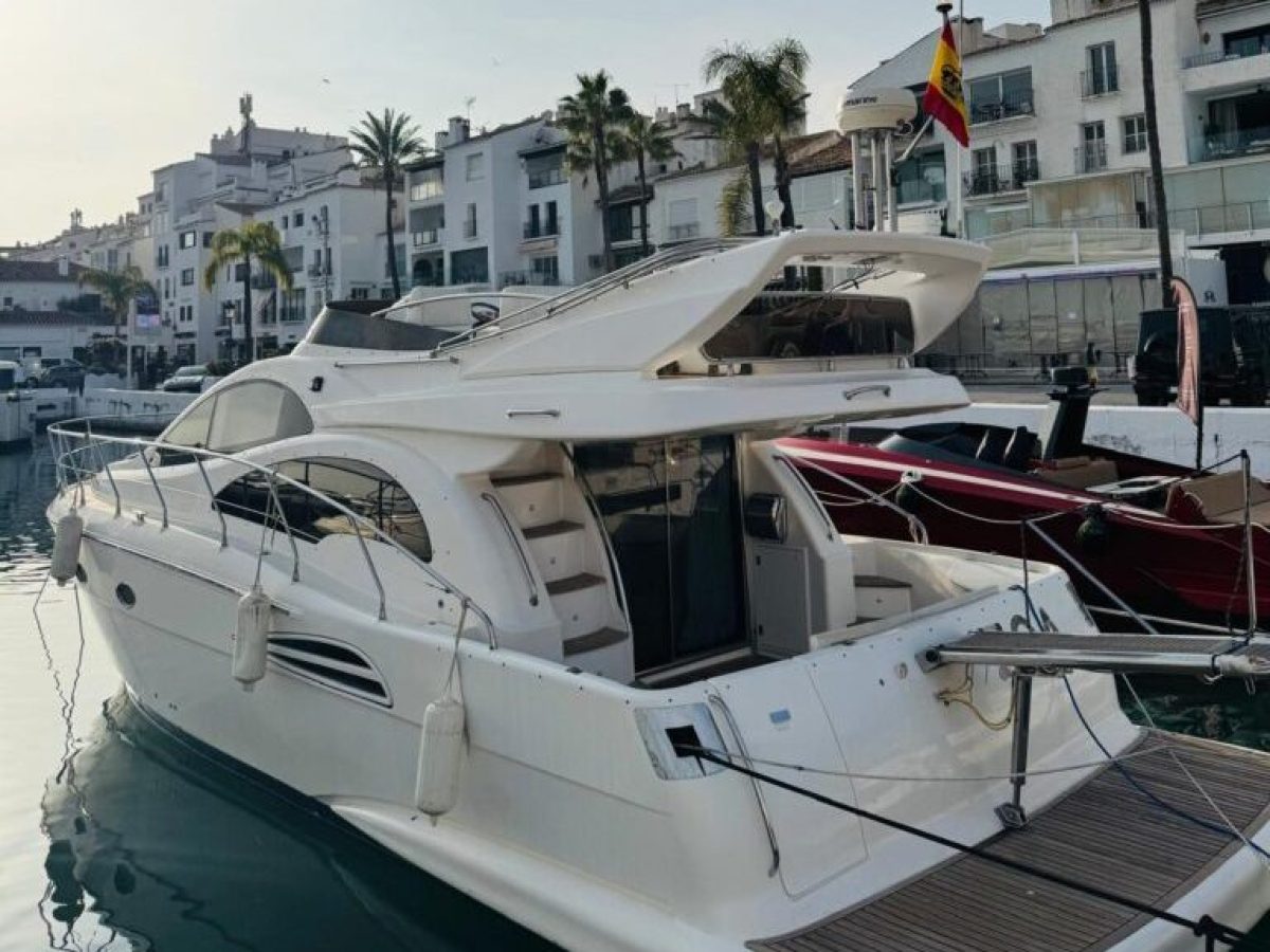 A luxury yacht docked in a marina with townhouses and palm trees nearby.