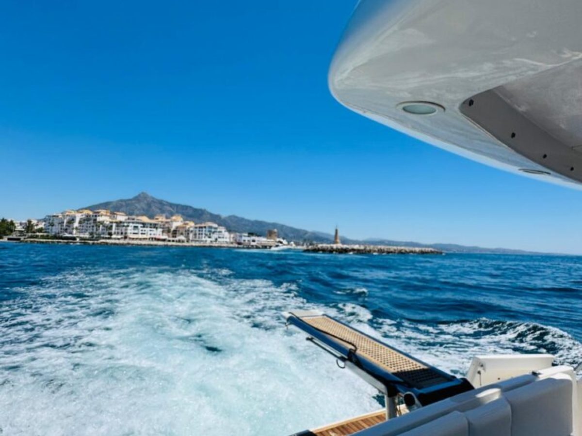 View from a boat's deck overlooking the sea and distant coastline on a clear, sunny day.