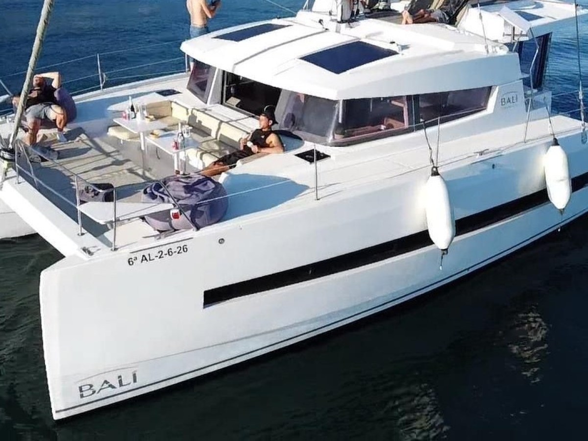 White catamaran yacht with people lounging on deck in calm waters.