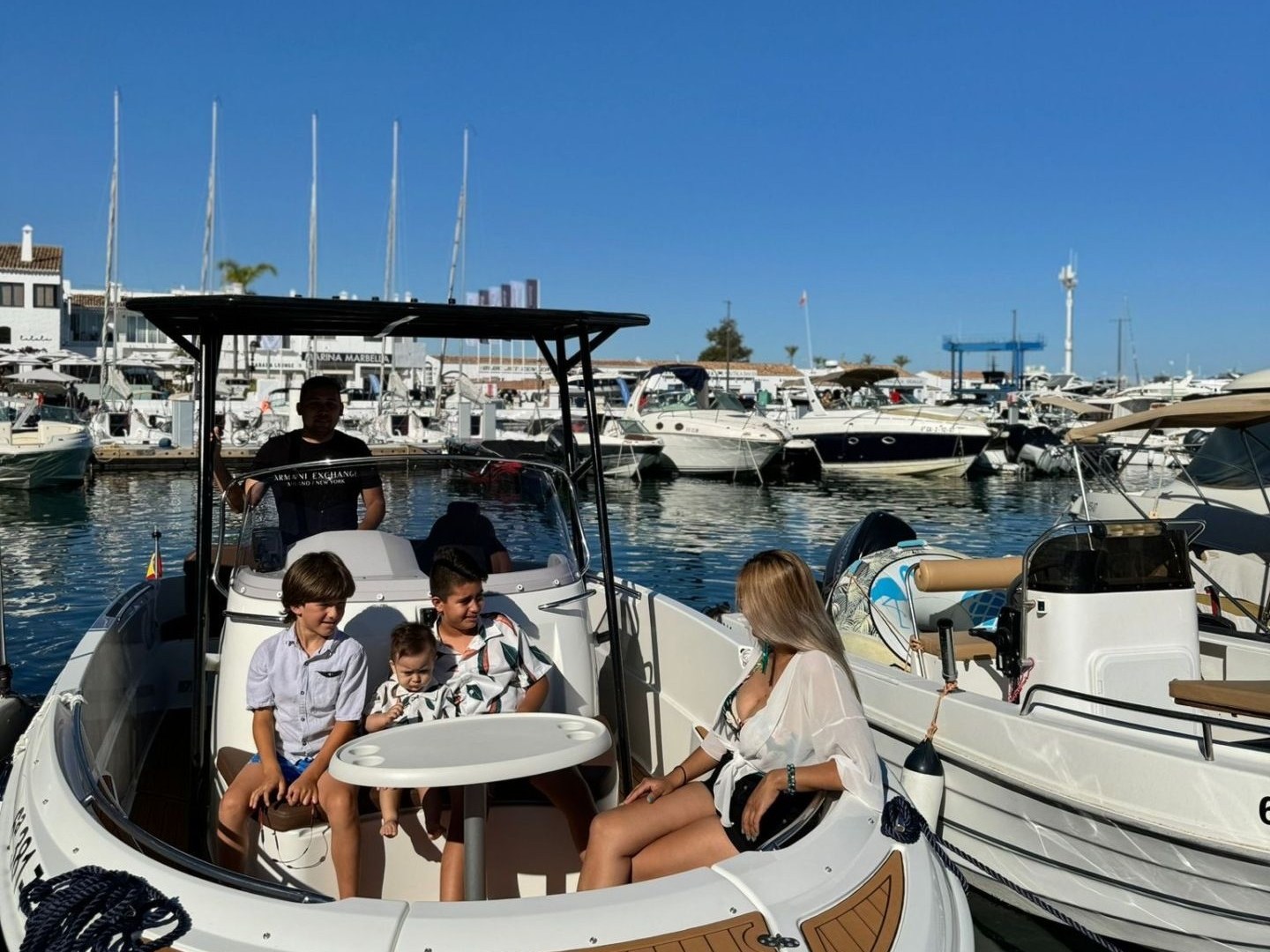 Family seated on a boat docked at a marina, under a clear blue sky.