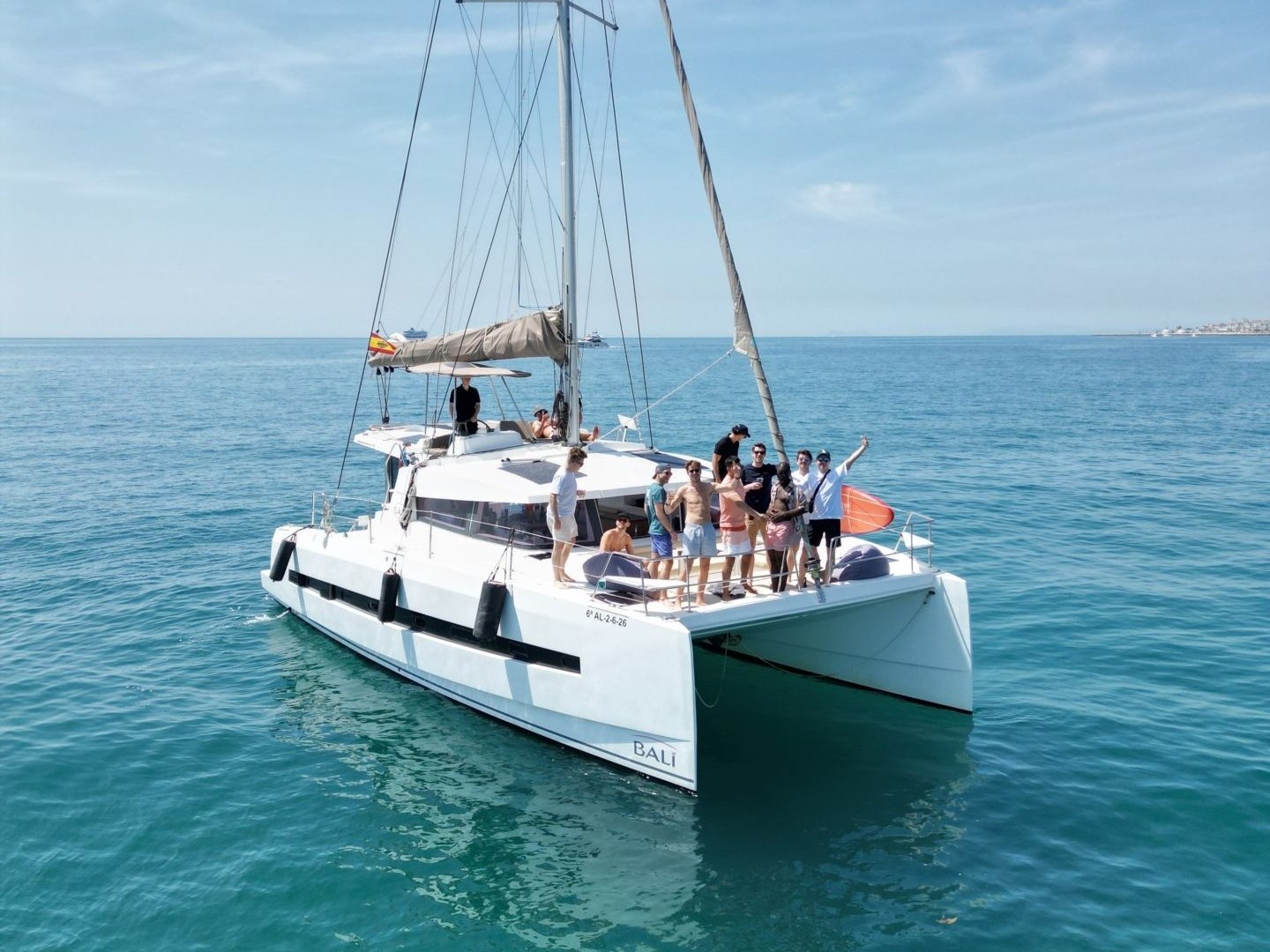 Catamaran with people sailing on calm blue sea under clear sky.