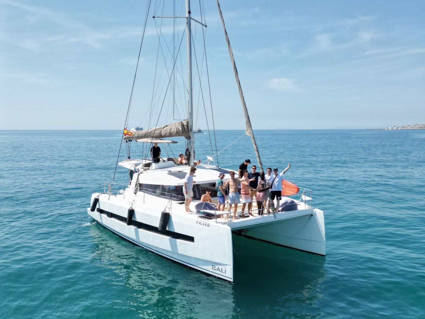 Catamaran with people on deck sailing in calm blue sea.