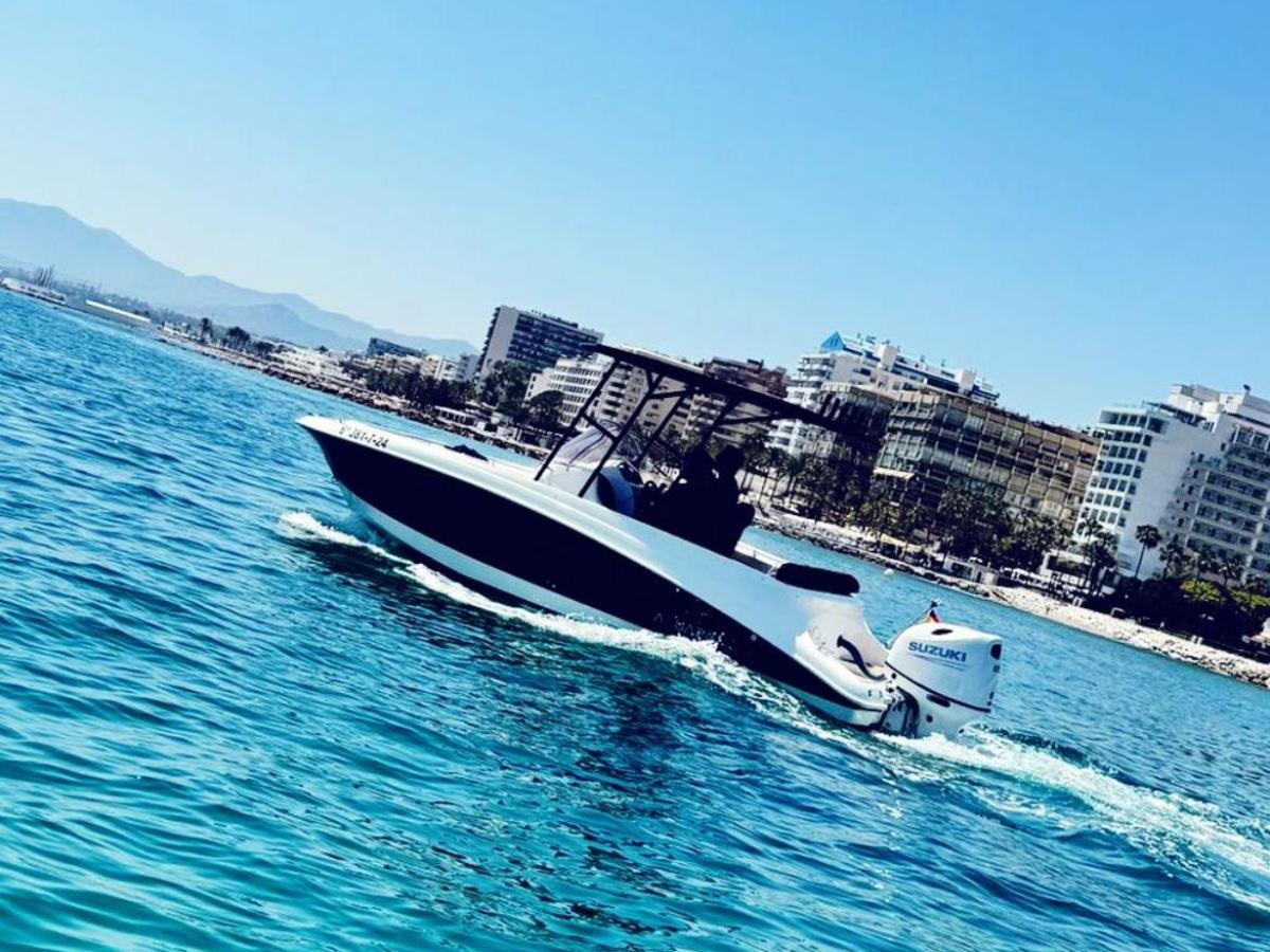 Small motorboat moving on a sunny ocean near a coastal cityscape.