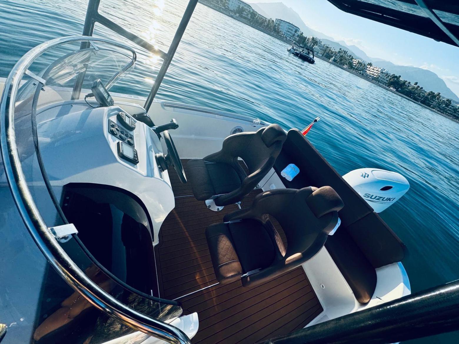 View of a small boat's seating area and control panel on a calm lake.