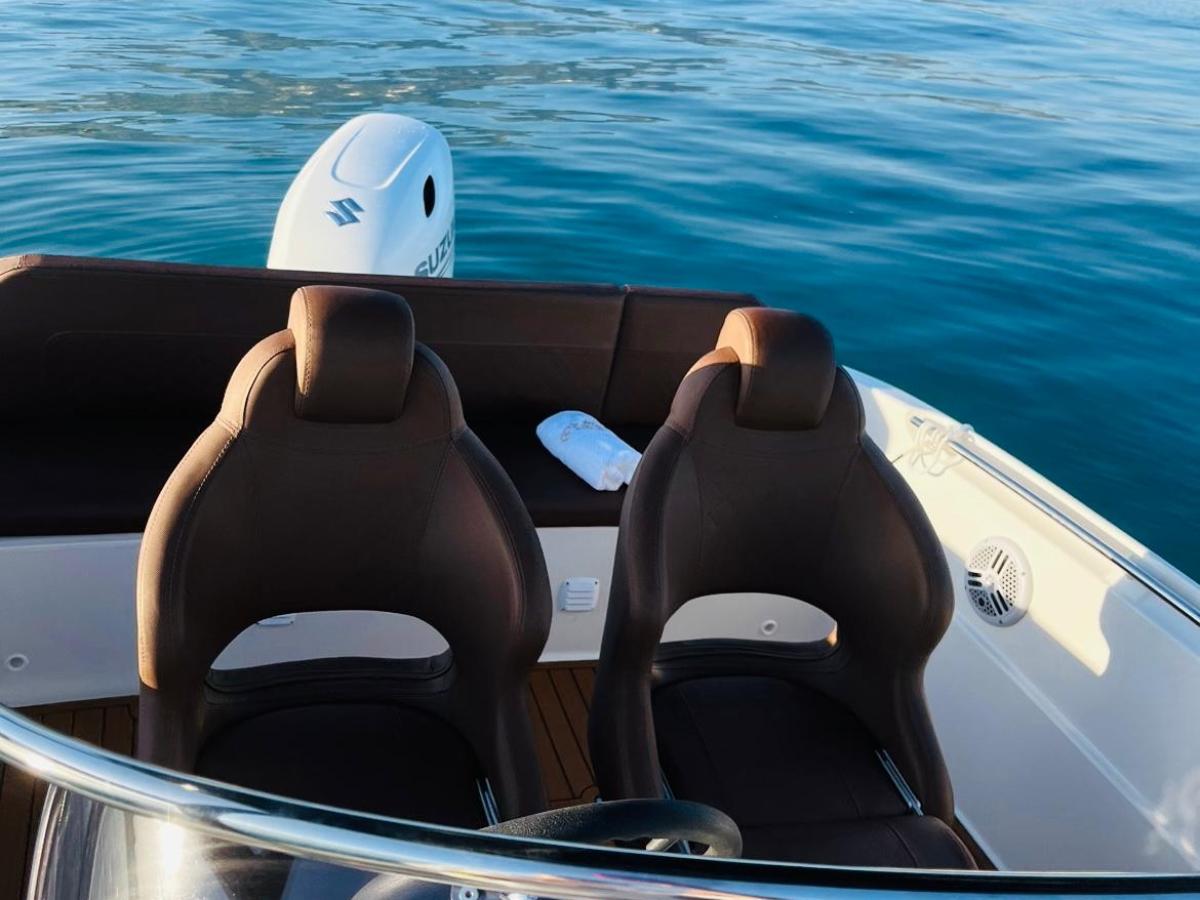 Boat cockpit with two seats facing calm blue water and distant mountains.