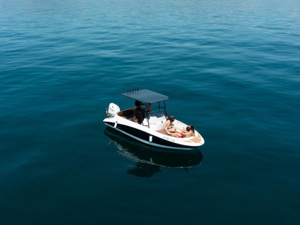 Small boat on calm, open water with a few people onboard.