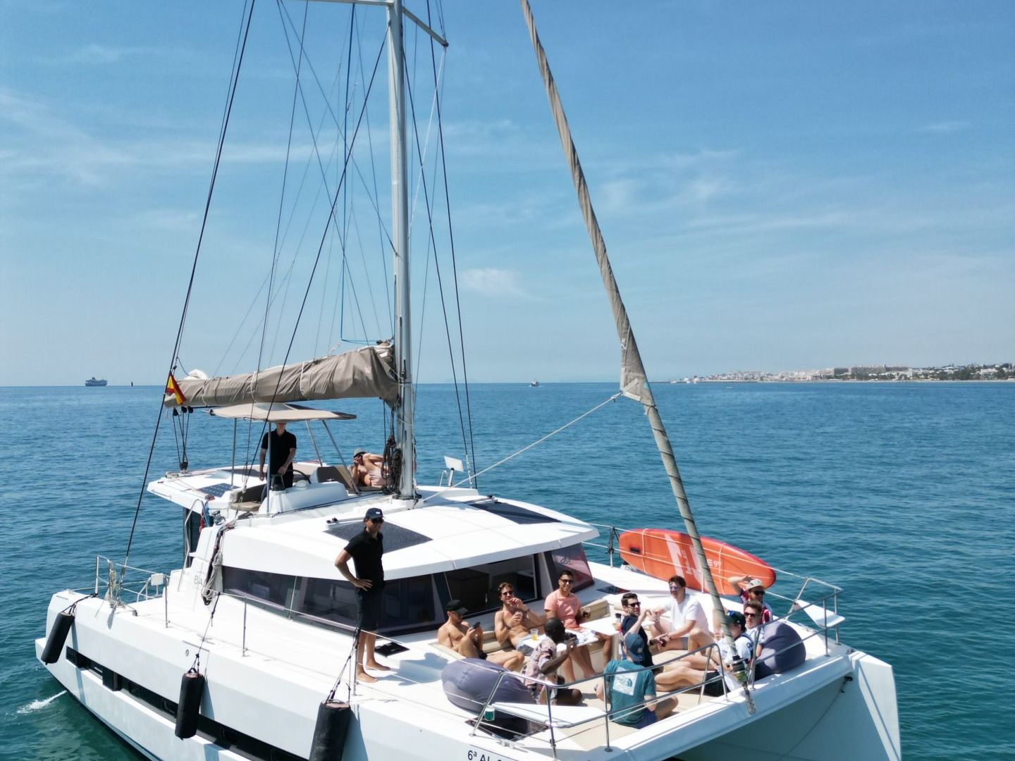 People relaxing on a white sailboat in clear blue waters under a sunny sky.