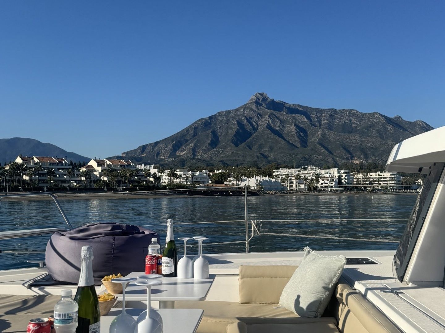 Yacht deck with drinks, snacks, and mountain view.