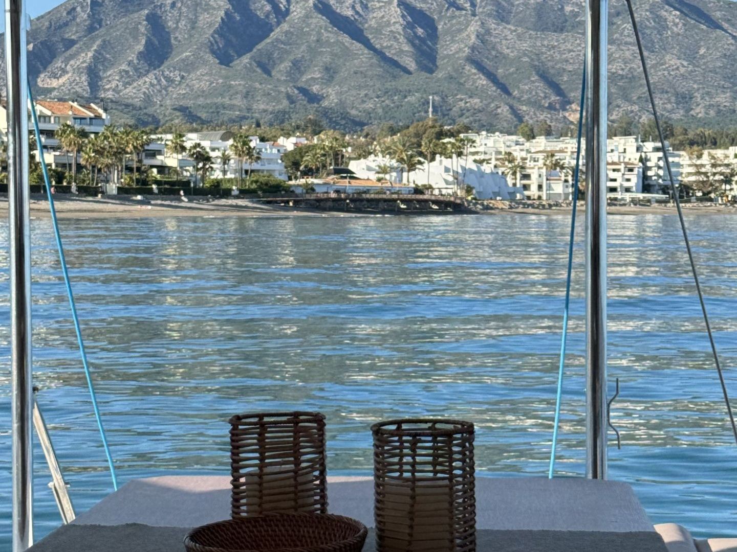 View of mountains and waterfront from a covered boat deck with a table and basket.
