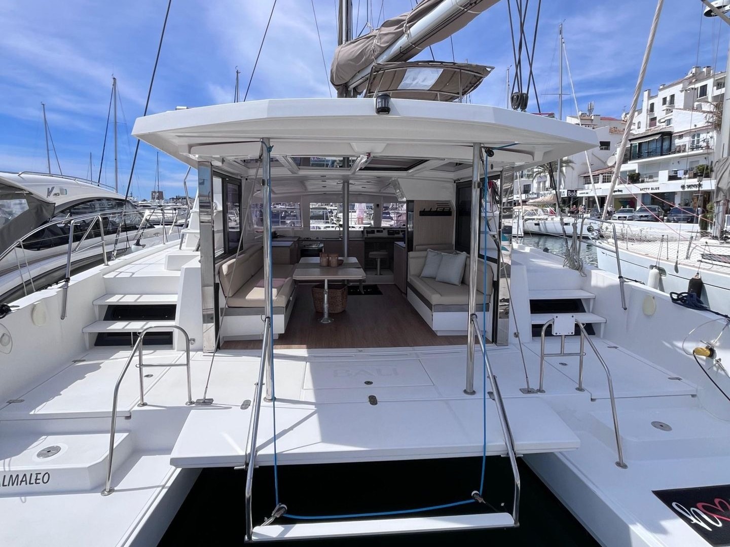 Stern view of a docked catamaran with an open cockpit and blue sky above.